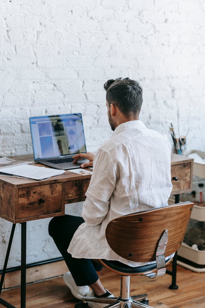 hero-img Back view unrecognizable male in formal wear working on modern netbook while sitting at desk in light room